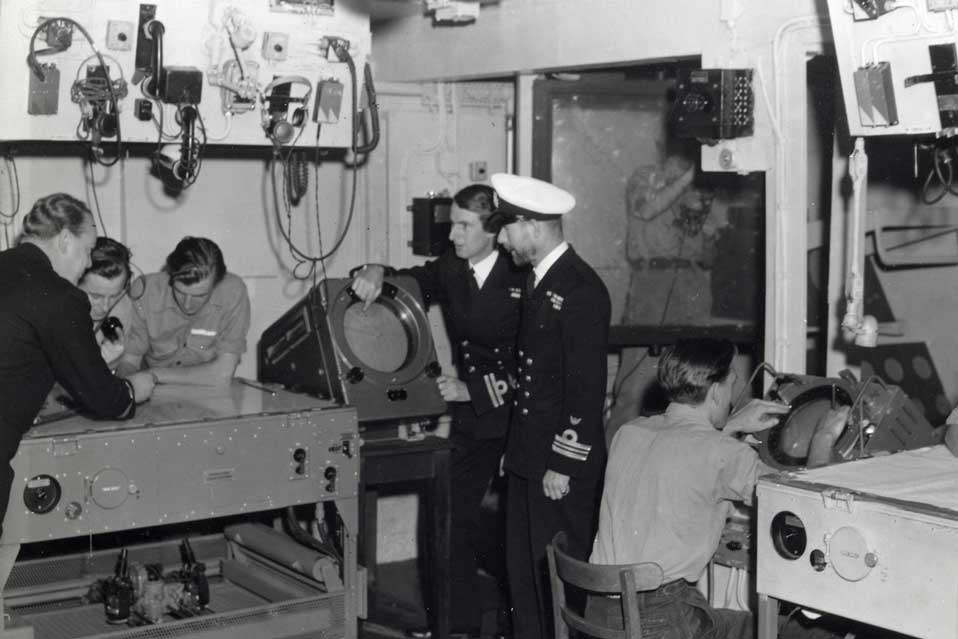 Personnel standing in a World War 2 era aircraft direction room
